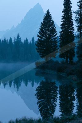 A blue hour water scene of lake, mountains, trees.