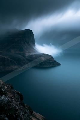 A blue hour long exposure water scene of ocean, mountains, lake.