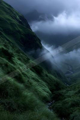 A moody landscape of mountains, valley, field.