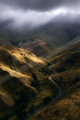A dramatic landscape of valley, mountains, road.