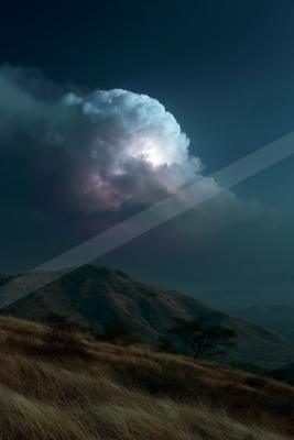 A massive, brightly illuminated cumulonimbus cloud with visible lightning flashes dominates a dark night sky above dry, rolling hills and savanna vegetation.