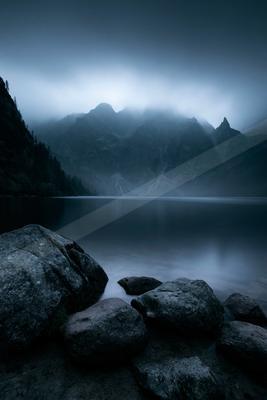 A blue hour long exposure water scene of lake, mountains, fog.