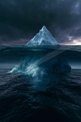A large white iceberg with its massive submerged portion visible beneath the dark ocean surface under a stormy sky