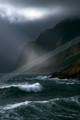 A moody water scene of ocean, beach, mountains.