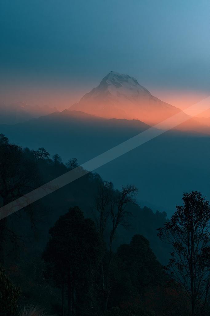 A blue hour landscape of mountains, sunrise, fog.