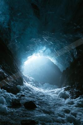 View from inside a dark blue ice cave looking toward a brightly lit opening, with snow and rocks covering the ground.
