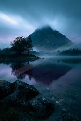 A blue hour water scene of lake, mountains, fog.