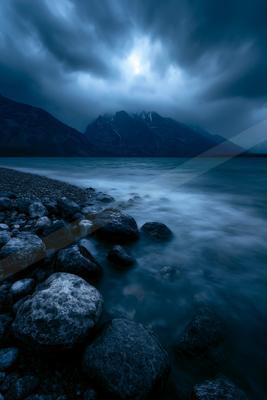 A blue hour long exposure water scene of lake, storm, mountains.