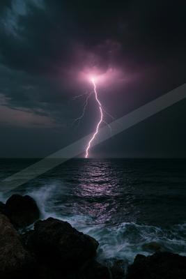 A bright pink and white lightning bolt strikes the ocean during a thunderstorm, illuminating dark clouds and creating a reflection on the turbulent water, with 
