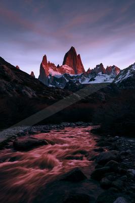 A moody landscape of mountains, river, waterfall.