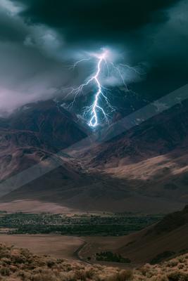 A powerful lightning bolt illuminates the night sky over rugged mountains and a valley below, creating a striking contrast against dark clouds.