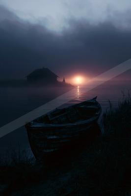 A weathered wooden rowboat rests on the grassy shore of a calm lake at dusk, with a small house and church steeple silhouetted in the foggy background under a g