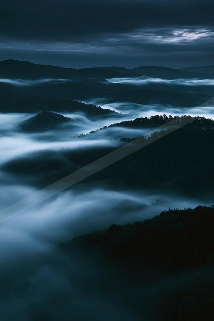 A blue hour long exposure landscape of mountains, valley, clouds.