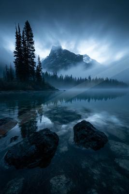 A blue hour long exposure water scene of lake, mountains, fog.