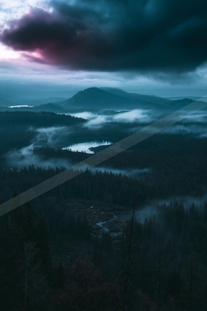 A blue hour landscape of mountains, valley, clouds.