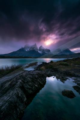 A serene lake reflects the rugged mountain peaks under a moody twilight sky.