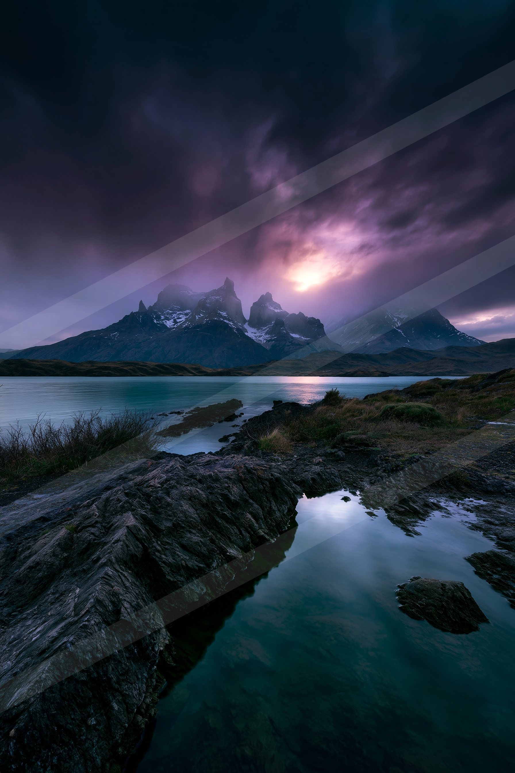 A serene lake reflects the rugged mountain peaks under a moody twilight sky.