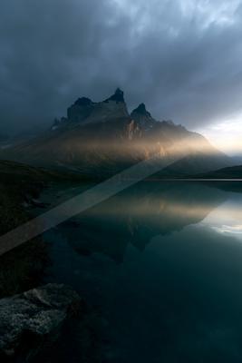 A blue hour water scene of lake, mountains, fog.