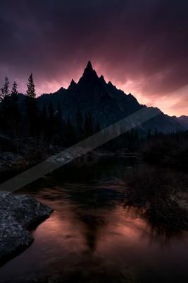 A jagged mountain peak rises against a dramatic purple and pink twilight sky, reflected in a calm river flowing through a dark forest with silhouetted trees and