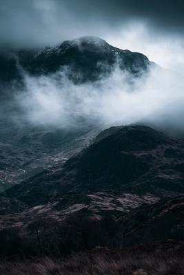 A dramatic landscape of mountains, fog.