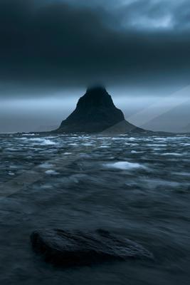 A dramatic water scene of ocean, storm, mountains.