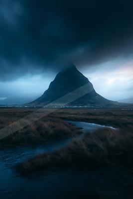 A blue hour landscape of mountains, storm, field.