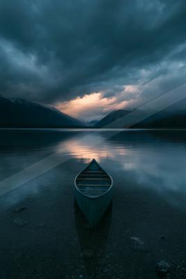A green-toned moody photograph of canoe, paddle, lakeside.