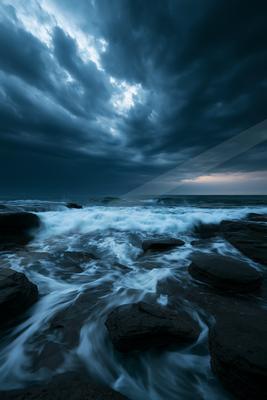A blue hour long exposure water scene of ocean, storm, rocks.