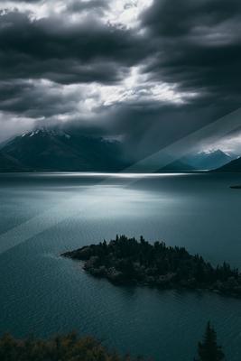 A moody landscape of mountains, storm, lake.