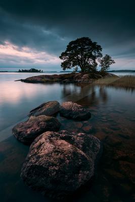 A blue hour long exposure water scene of lake, trees, rocks.