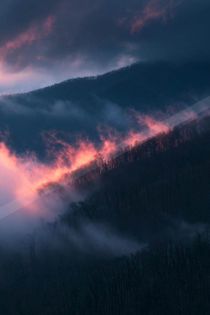 A dramatic sky scene of sunrise, mountains, clouds.