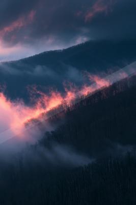 A dramatic sky scene of sunrise, mountains, clouds.