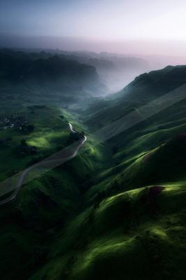 A moody landscape of valley, field, mountains.