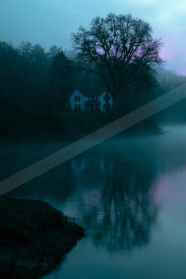 A white house stands on a foggy riverbank beside a large bare tree, its reflection visible in the calm water under a blue and purple dawn sky.