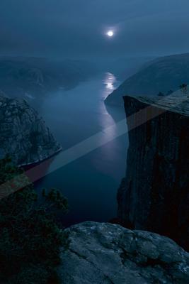 A dramatic night view of a deep fjord with steep rocky cliffs under a bright full moon, its light reflecting on the calm water surface, surrounded by misty moun