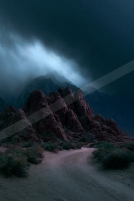 Moody atmospheric scene of rugged red rock formations in a desert landscape under heavy dark storm clouds with a band of blue light breaking through, a sandy pa