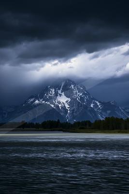 A dramatic landscape of mountains, storm, lake.