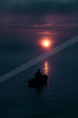 A silhouetted person sits in a small boat on calm water, facing a bright sun rising through thick fog with dramatic purple and pink colors in the sky.