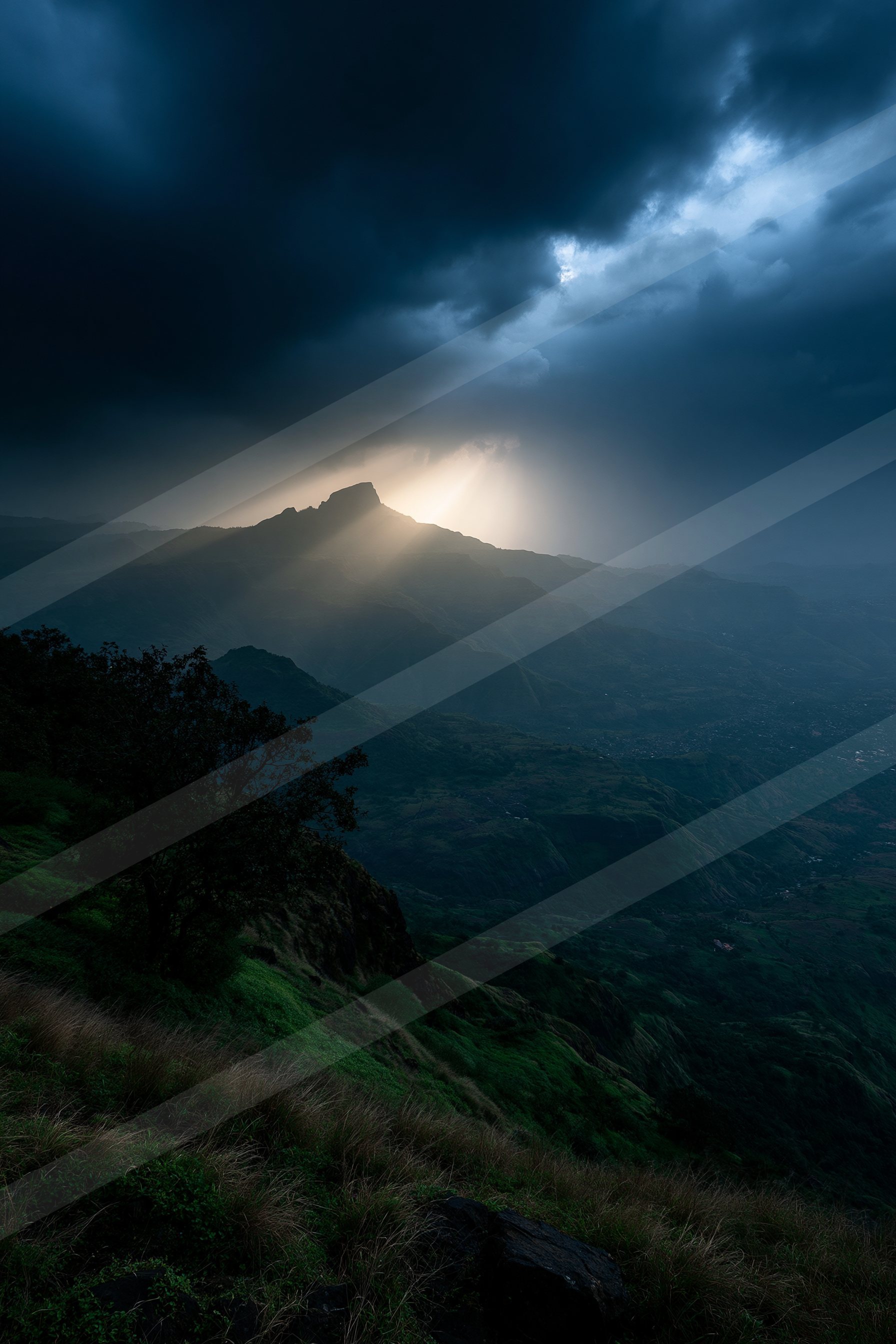 A mountain peak is illuminated by moonlight piercing through dark clouds, casting a dramatic glow over the surrounding landscape.