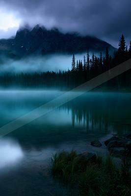 A blue hour long exposure water scene of lake, mountains, fog.