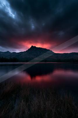 A moody water scene of lake, sunset, mountains.
