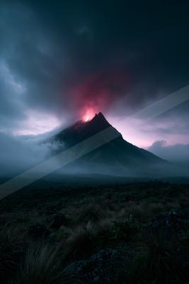 A powerful volcanic eruption with bright red lava and glowing plume rising from the peak of a dark mountain, surrounded by thick clouds and mist at dusk, with a