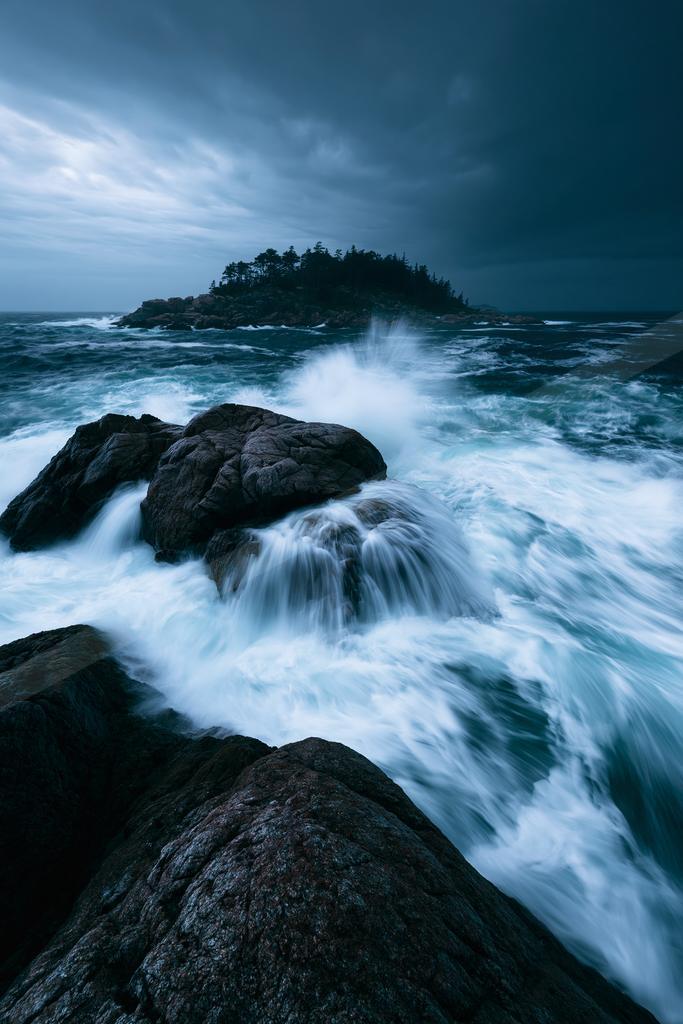 A blue hour long exposure water scene of ocean, storm, rocks.
