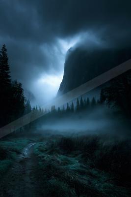 A winding dirt path leads through a misty meadow toward a towering mountain partially obscured by thick fog and dramatic storm clouds in a dark, atmospheric lan
