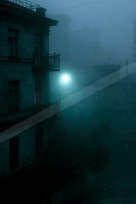 A foggy night scene in an old urban neighborhood, featuring weathered apartment buildings with balconies, a bright glowing streetlamp cutting through dense blue