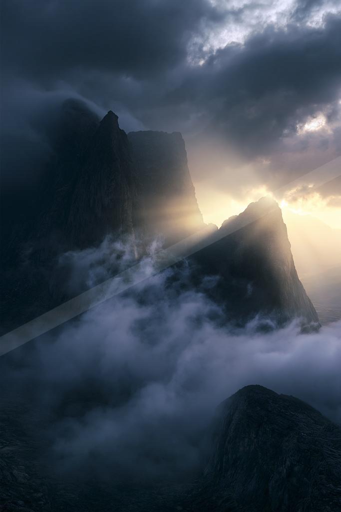 A dramatic landscape of mountains, clouds, fog.