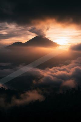 A dramatic landscape of mountains, sunrise, clouds.
