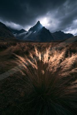 A dramatic long exposure landscape of mountains, field, storm.