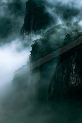 A dramatic landscape of mountains, ocean, fog.