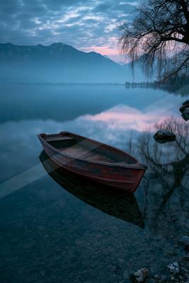 A black-toned moody photograph of lakeside, canoe, boathouse.